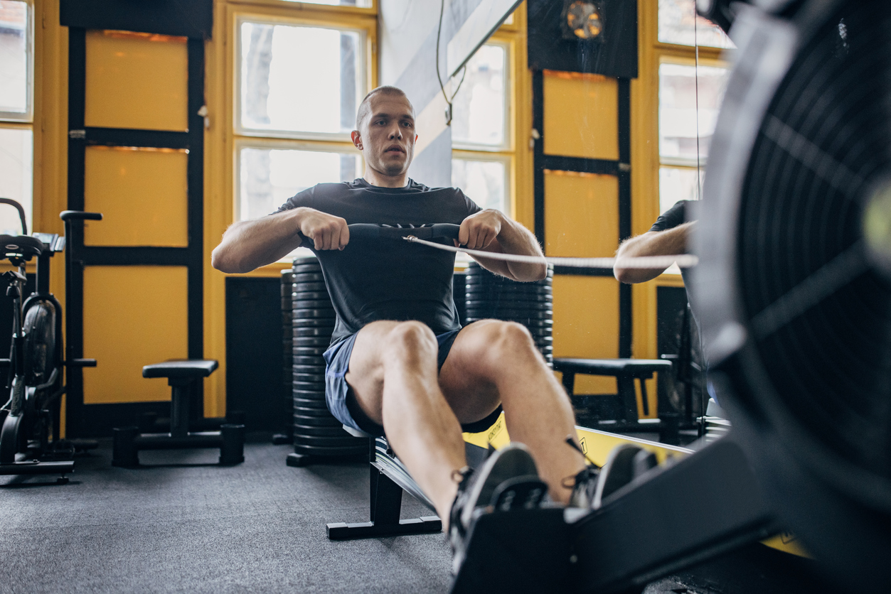 One man, fit man exercising on rowing machine in gym alone.